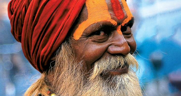 Portrait en gros plan d'un sadhou souriants avec un maquillage facial orange vif et un turban rouge.