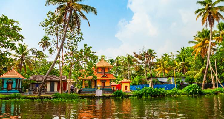 Colorful village houses and temples reflected in lush Kerala backwaters amid palm trees.