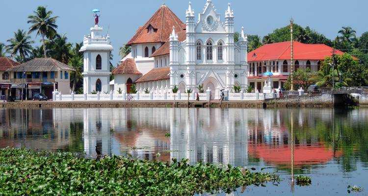 White colonial church reflected in tranquil lagoon waters surrounded by tropical greenery in Kerala.