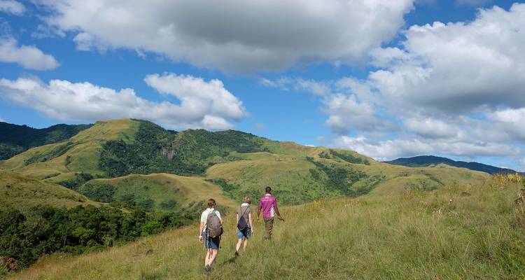 Small group hikes along rolling grassy ridges under dramatic cloud-dotted skies in Fiji’s highlands.
