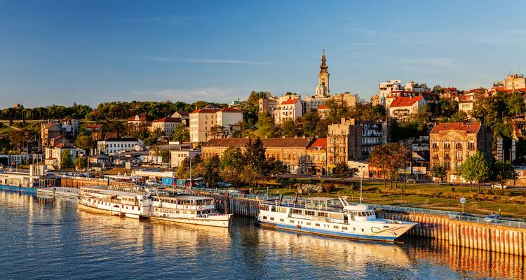 Evening light warms Belgrade’s waterfront skyline where river cruise boats dock along the quay.
