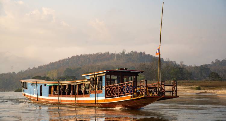 Croisière traditionnelle en bateau long sur le Mékong avec le drapeau du Laos au crépuscule.