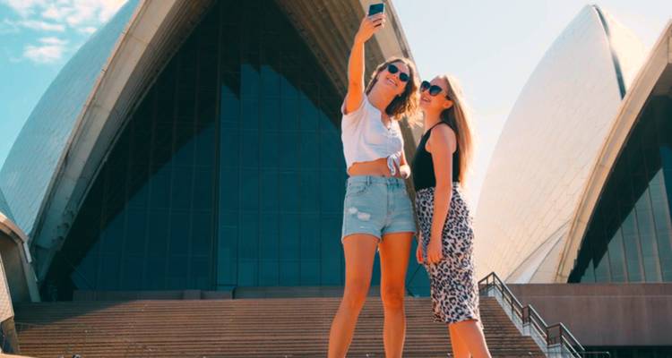 Two young women pose for a selfie on the steps in front of the Sydney Opera House.