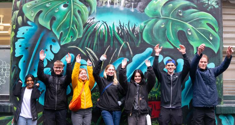 Cheerful group of travellers with arms raised in front of a colourful tropical street-art mural