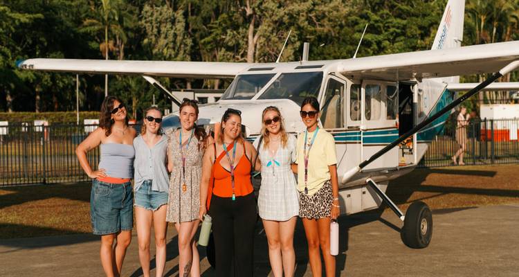 Group of women standing in front of a small propeller plane on a sunny airfield