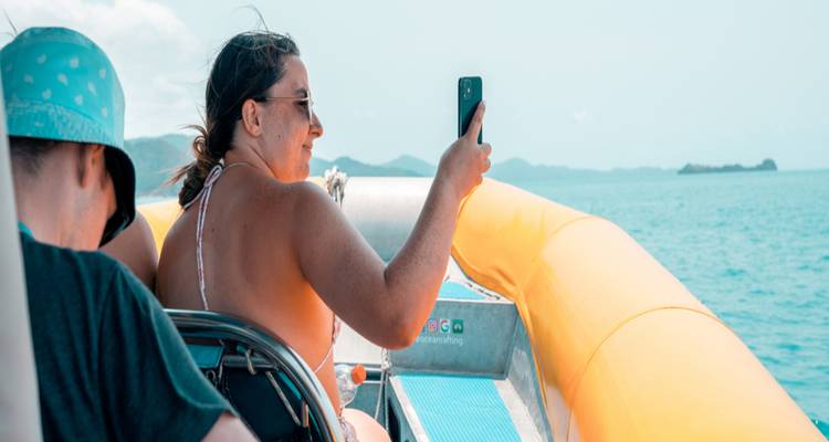Woman taking a smartphone photo from an inflatable boat speeding across bright blue seas