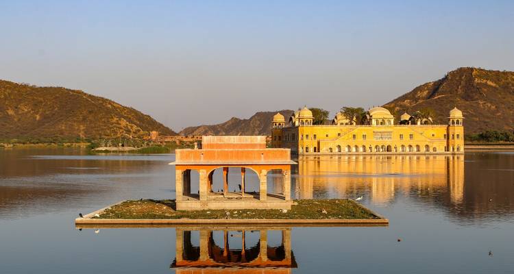 Lac serein reflétant le palais doré de Jal Mahal et les collines arides environnantes à la lumière de fin d'après-midi.