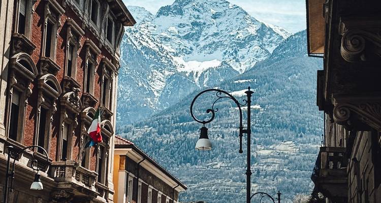 Malerische Stadtstraße mit kunstvollen Gebäuden, die sich vor einer dramatischen schneebedeckten Bergkulisse erstreckt.