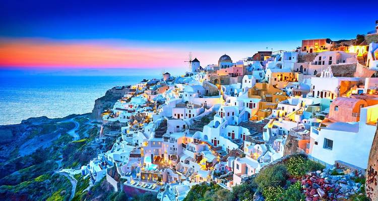 Twilight panorama of Santorini’s Oia village glowing with pastel buildings against a deep blue sky.