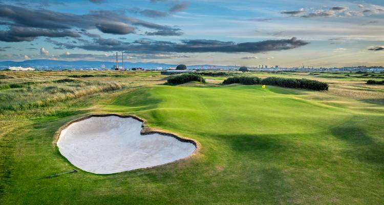 Breite grüne Fairway und Sandbunker eines Küsten-Linksgolfplatzes in Irland in der Abenddämmerung.