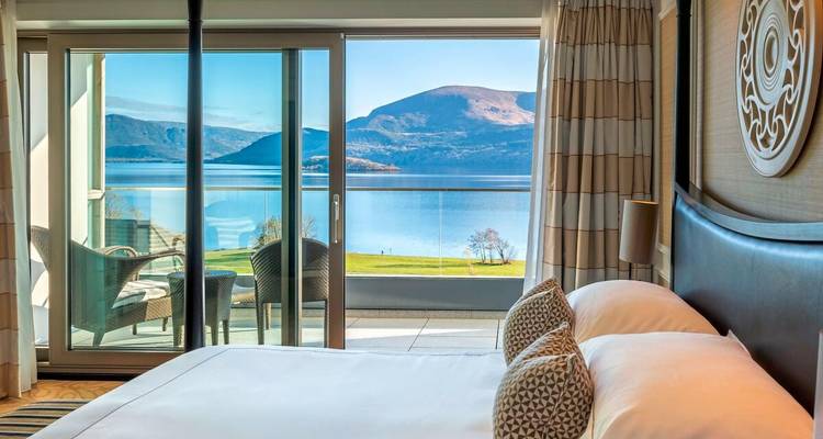 Habitación de lujo en hotel con balcón y vista al lago y las montañas a través de puertas corredizas.