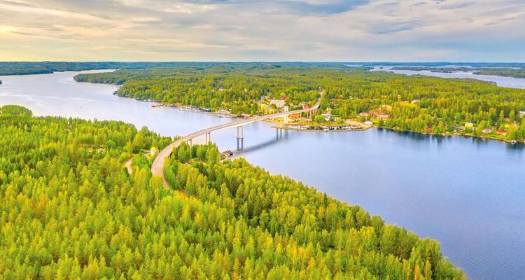 Lange Betonbrücke, die über einen glitzernden See und dicht bewaldete grüne Inseln in Finnland führt.