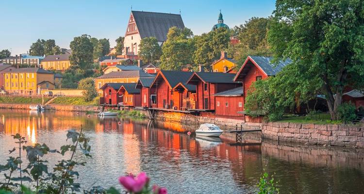 Charmante rote Flussuferlagerhäuser und historische Kirche des Alten Porvoo, die sich im Abendlicht spiegeln.