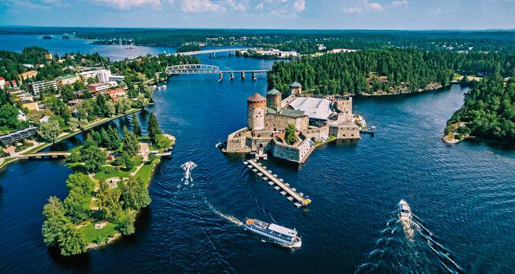 Dramatische Luftaufnahme des mittelalterlichen Schlosses Olavinlinna auf einer Insel inmitten eines tiefblauen finnischen Sees mit Booten.