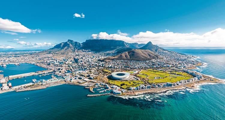 Spektakuläre Luftaufnahme von Kapstadt, dem Tafelberg und einem Stadion zwischen Ozeanbucht unter hellem Himmel.