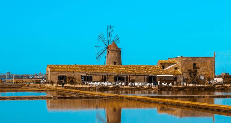 Traditionelle Windmühle spiegelt sich in glitzernden Salzbecken unter einem leuchtend blauen Himmel.