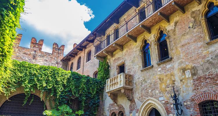 Patio de ladrillos con paredes cubiertas de hiedra y el famoso balcón de Julieta en Verona bajo un cielo despejado.