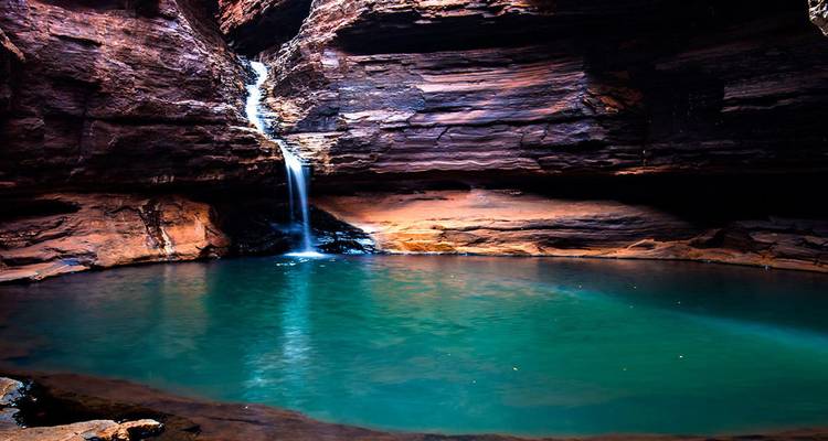 Secluded emerald pool fed by a thin waterfall within the red-walled gorges of Karijini National Park.