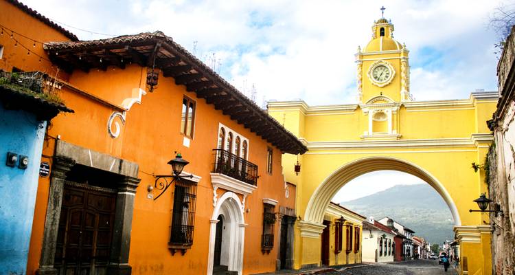 Un icónico arco amarillo con torre de reloj se extiende sobre una colorida calle colonial que lleva a un volcán.