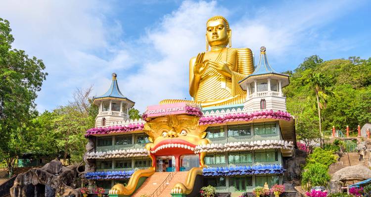 The giant gilded Buddha and lion-mouth entrance of Dambulla’s Golden Temple complex against blue sky.