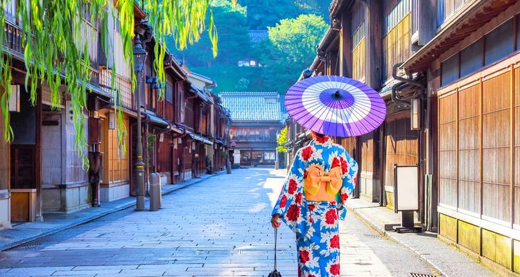 A woman in vibrant yukata with parasol strolls a quiet traditional wooden street lined with teahouses.