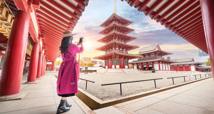 Traveler photographing the five-story pagoda of Senso-ji temple framed by red pillars at colorful sunset.