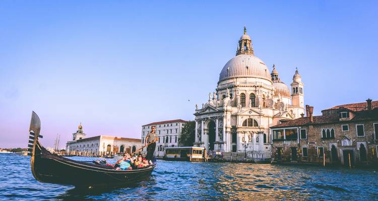 Een gondel glijdt voorbij de koepelvormige Basilica di Santa Maria della Salute op Venetiës Grand Canal in gouden middaglicht.