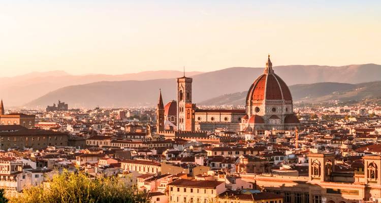 Panoramisch uitzicht op Florence met de rode pannendaken van de Duomo en Giotto's campanile die boven de stad uitsteken in het warme licht van de zonsondergang.