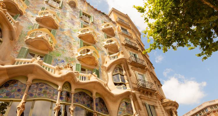 Fachada colorida y curva de la Casa Batlló de Gaudí vista desde el nivel de la calle en un día soleado.