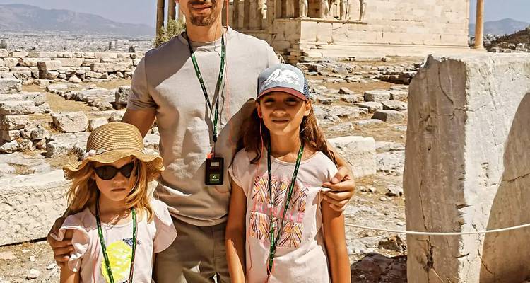 Vater und zwei Kinder posieren zwischen antiken Ruinen auf dem Akropolis-Hügel in heller Sonne.