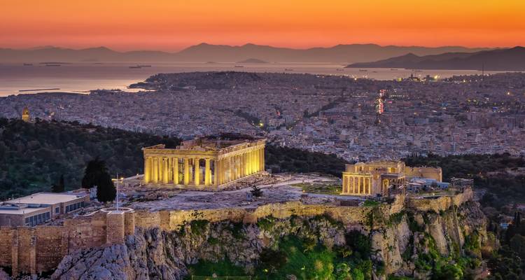 L'Acropole illuminée couronne Athènes au coucher du soleil avec la ville et la mer au-delà.