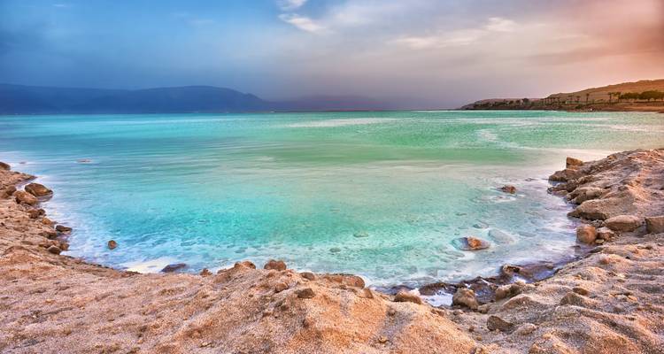 Les eaux turquoise de la mer Morte qui viennent lécher le rivage sablonneux riche en minéraux sous un ciel brumeux.