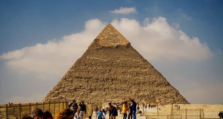 Menschenmengen nähern sich der riesigen Großen Pyramide unter einem teilweise bewölkten Himmel, was ihre majestätische Größe unterstreicht.