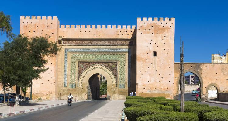 Das Bab-Mansour-Tor in Meknes mit aufwändigen Zellijfliesen und aufragenden Lehmziegelmauern vor tiefblauem Himmel.