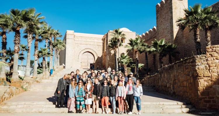 Large tour group poses on stone steps beneath palm trees at the Kasbah of the Udayas.