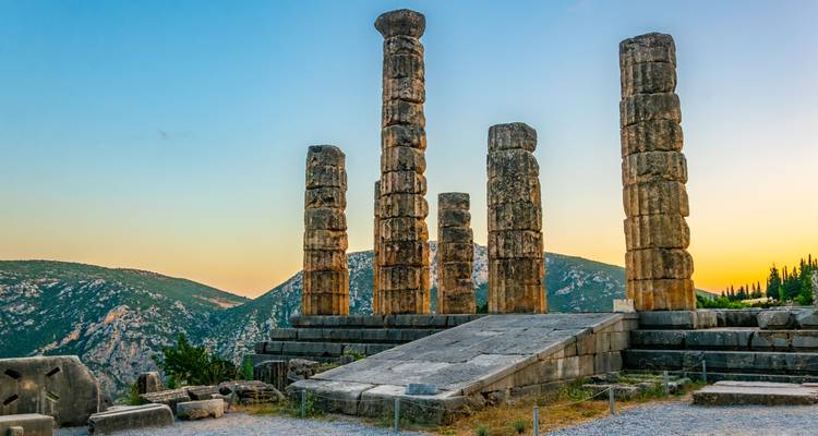 Standing columns of the Temple of Apollo at Delphi at sunset with rolling hills behind.