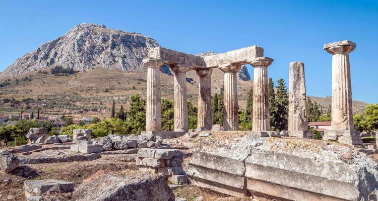 Ruins of ancient Doric columns of Corinth set before a craggy mountain under clear skies.