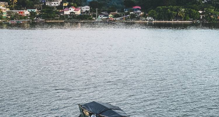 Escena tranquila de un lago con una pequeña barca cubierta y casas coloridas a lo largo de la orilla lejana.