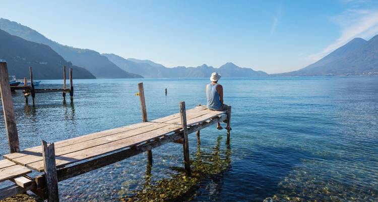 El viajero se sienta al final de un muelle de madera mirando hacia las aguas azules del Lago Atitlán.