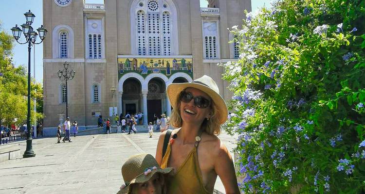 Mère et enfant portant des chapeaux de soleil souriant devant une église historique ornée d'icônes en mosaïque.