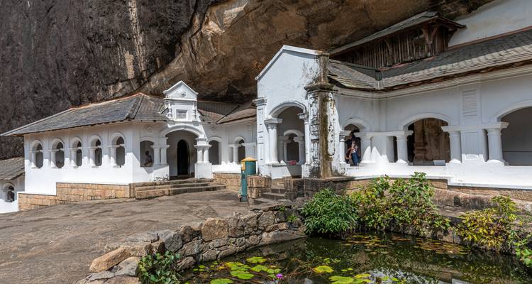 Los edificios del monasterio con arcos blancos se aferran a la cara de una roca junto a un estanque de lirios en Dambulla.