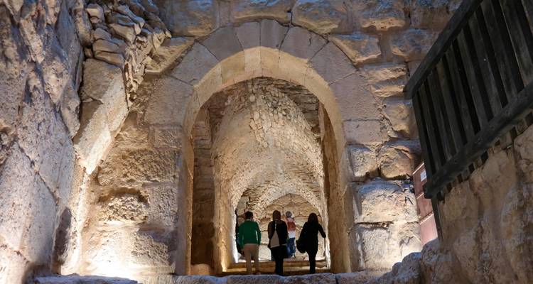 Visitantes caminando por un corredor con arcos de piedra dentro de un antiguo castillo en la cima de una colina