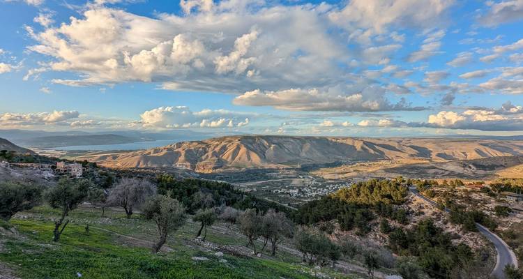 Vue panoramique d'une vallée avec des champs en patchwork, une route sinueuse et un ciel spectaculaire rempli de nuages