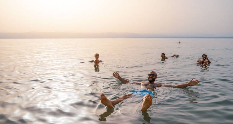 Les voyageurs flottent sans effort sur les eaux calmes et brumeuses de la mer Morte au coucher du soleil.