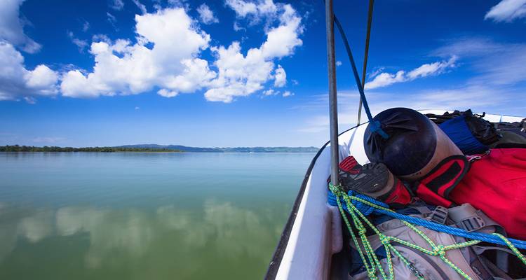 La proa de un bote lleno de equipo apunta hacia un lago enorme y cristalino bajo cielos azules.