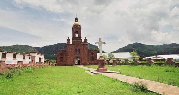 Iglesia de ladrillo de la misión con campanario ubicada en un patio abierto y herboso contra cielos nublados y colinas
