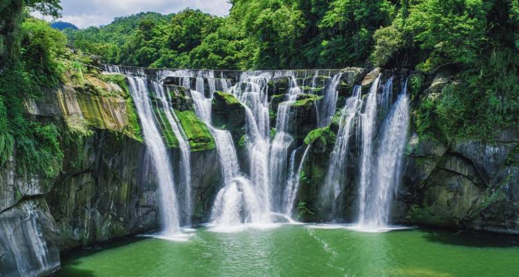 Powerful multi-tiered waterfall cascading into a green pool surrounded by lush forest