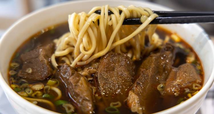 Hearty Taiwanese beef noodle soup with thick noodles lifted by chopsticks