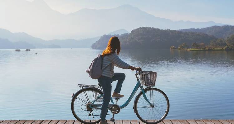 Cyclist on a boardwalk gazes over tranquil Sun Moon Lake and misty mountains