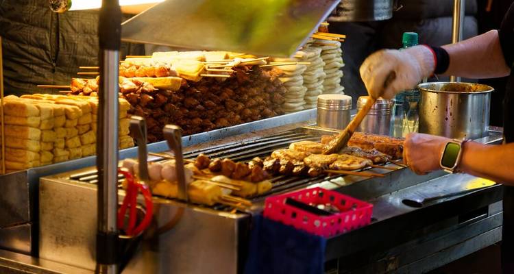 Vendor grills skewers and stacks fried treats at a bustling night market stall